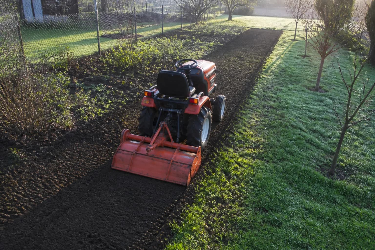 Kompaktný malotraktor so zadným rotavátorom pracuje v menšej záhrade.