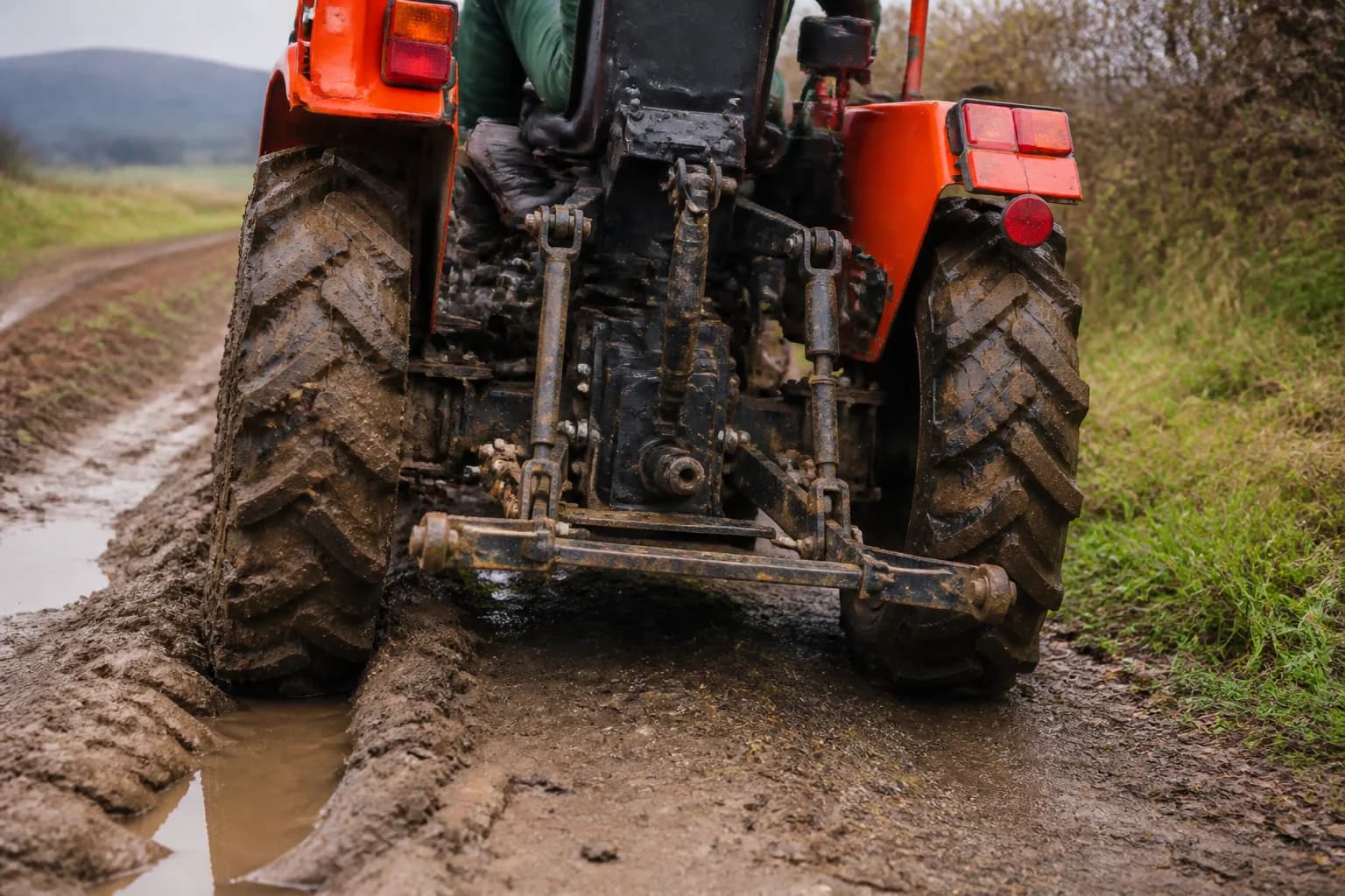Malotraktor s detailom zadných kolies pracuje na mokrej poľnej ceste s vyjazdenými koľajami.