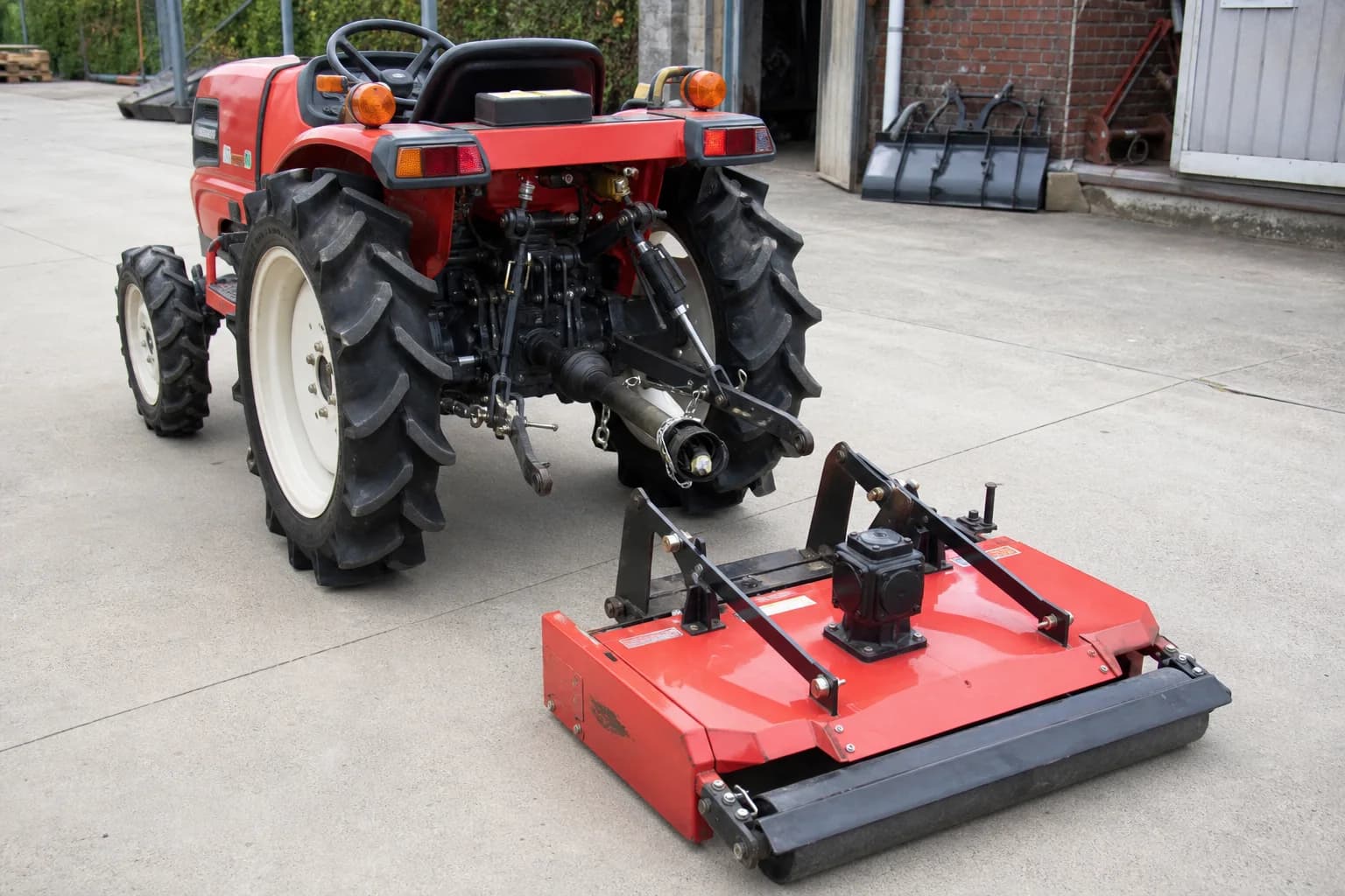 Malotraktor na rovnom betónovom povrchu stojí pred zadnou kosačkou pripravenou na pripojenie.
