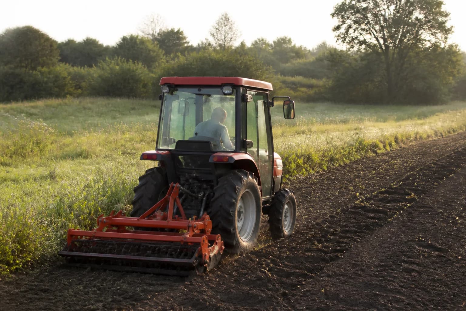 Malotraktor s pripojenými bránami pracuje na okraji poľa pri lúke.