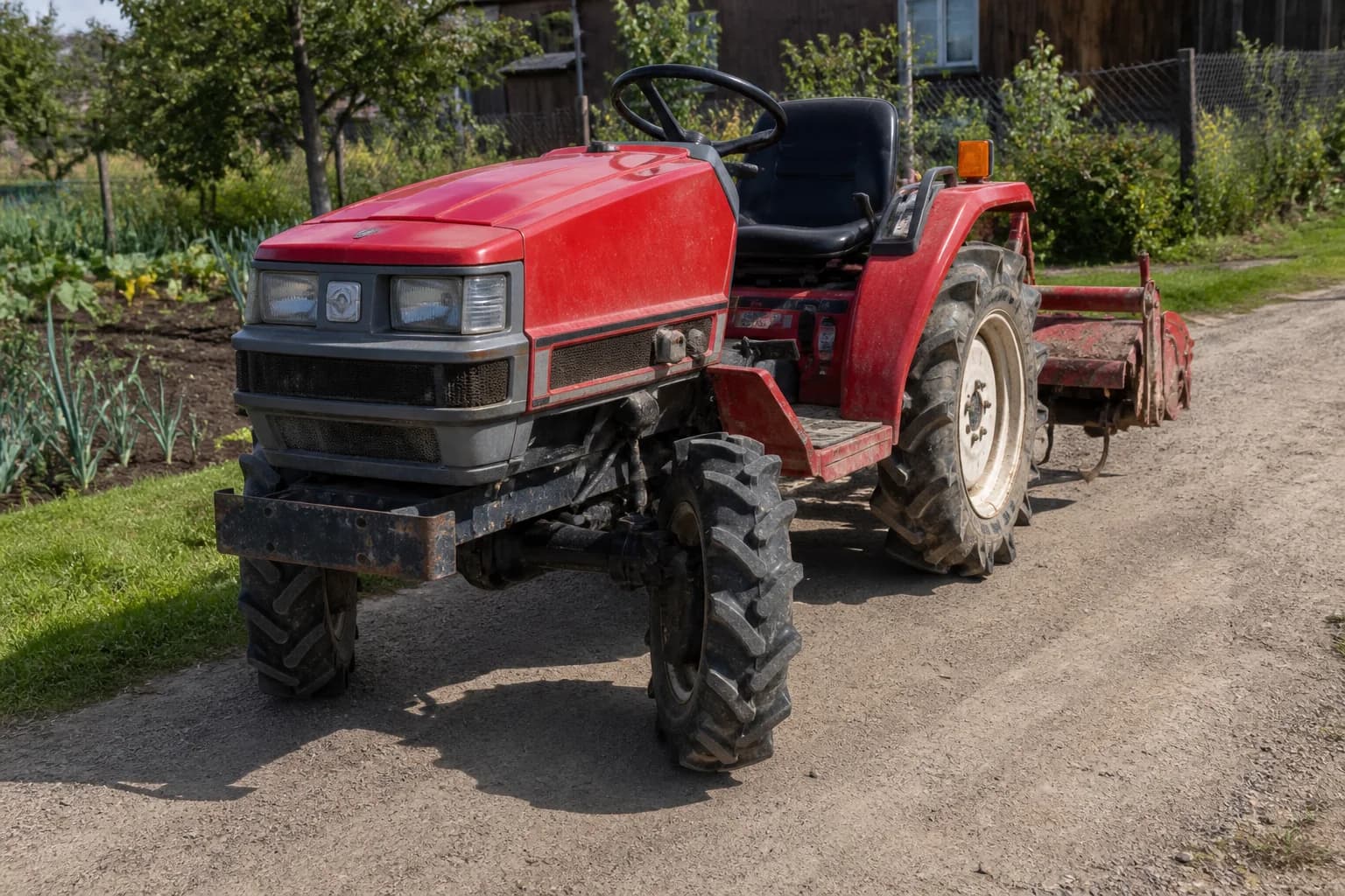 Malotraktor na poľnej ceste s viditeľnými prednými kolesami a pripojeným náradím.