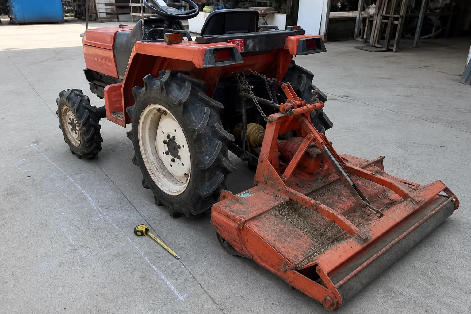 Malotraktor s pripojenou rotačnou kosačkou stojí na rovnej ploche pri meraní záberu.