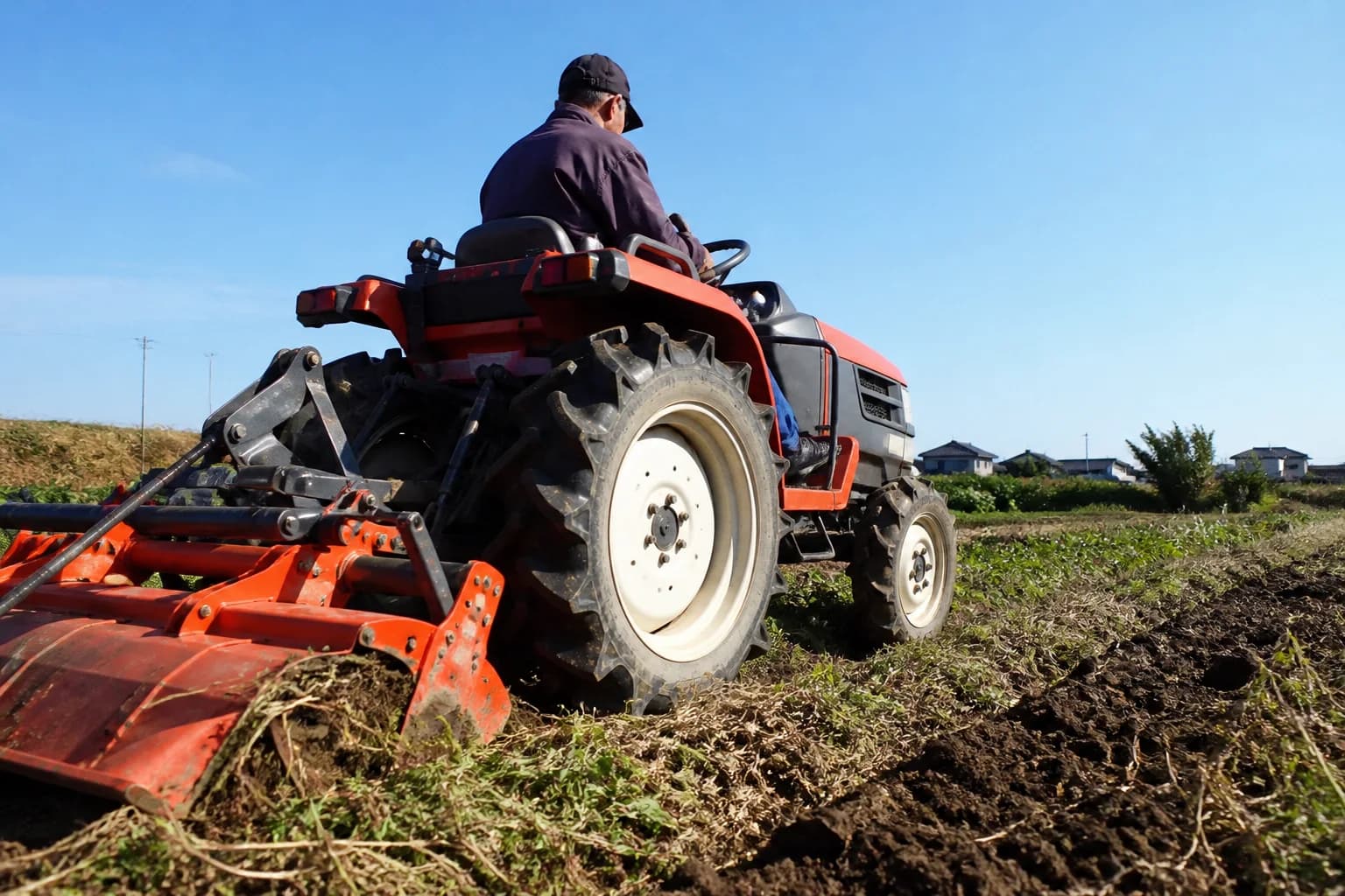 Kompaktný malotraktor pracuje pomaly s pôdnym náradím na menšom poli.