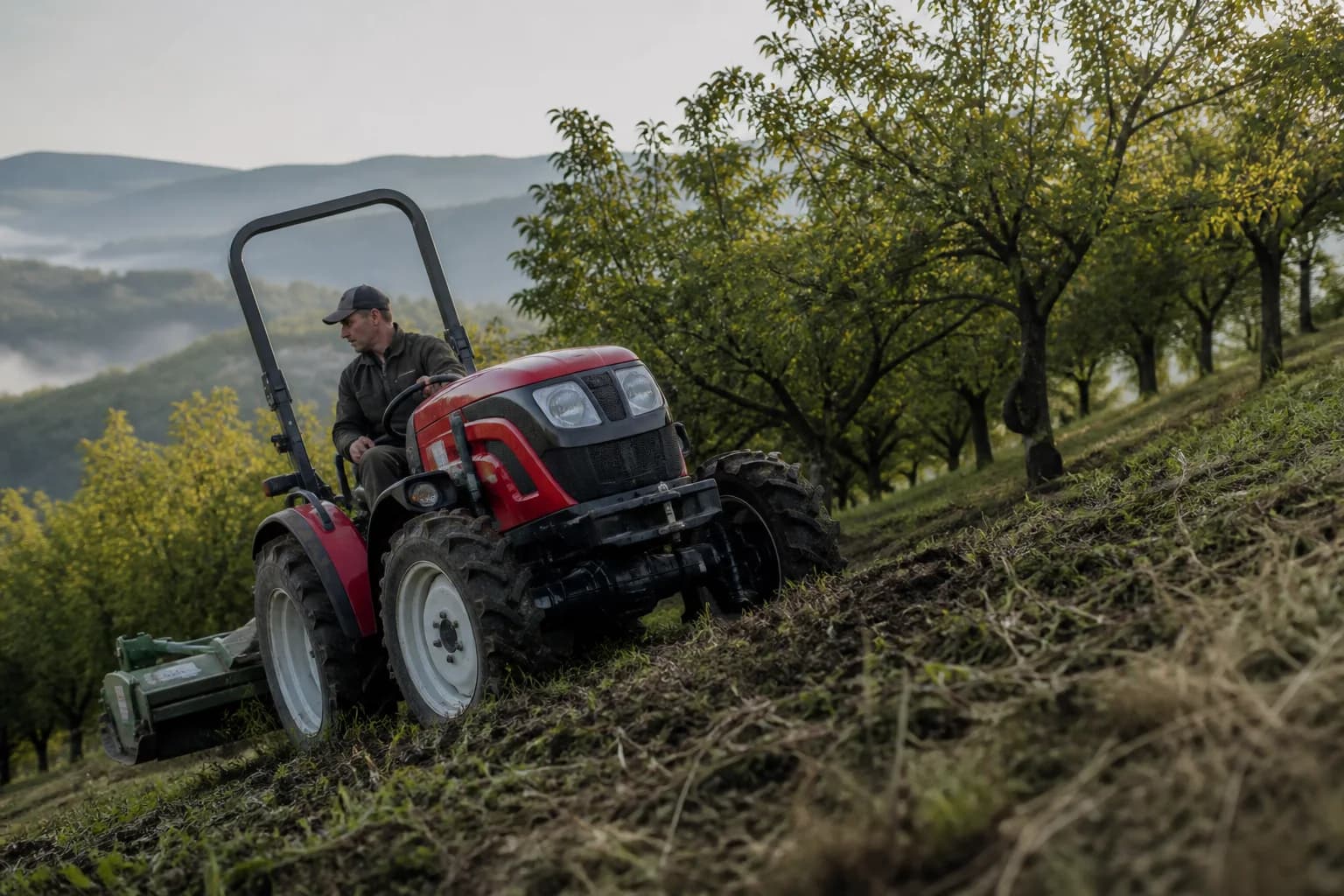 Kompaktný malotraktor s pohonom 4x4 pracuje na svahovitom pozemku pri sade.